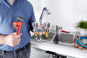 Hands of professional Plumber with a water tap and wrench.